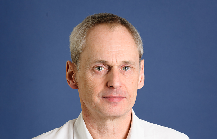 A professional man in a white shirt stands against a blue background, representing the corporate