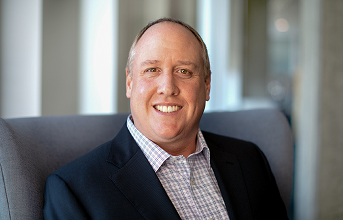 A professional individual dressed in a business suit with a checkered shirt sits comfortably on