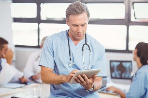 A healthcare professional in scrubs and a stethoscope is focused on a tablet