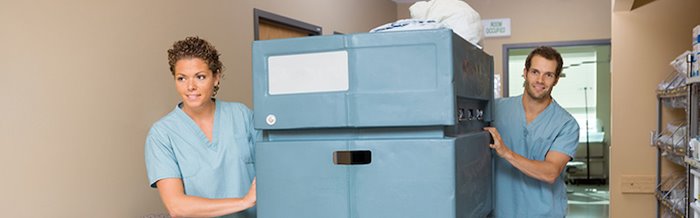 Healthcare staff maneuvering a wheeled linen bin in a hospital, reflecting Impinj's efficiency in healthcare operations.