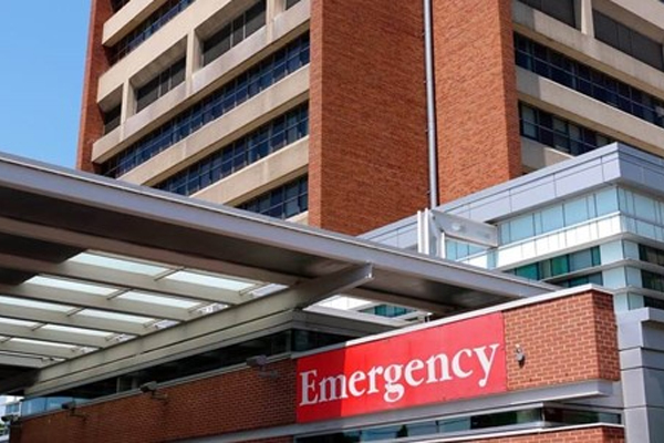 The image showcases the exterior of a modern hospital building with a prominent red sign that