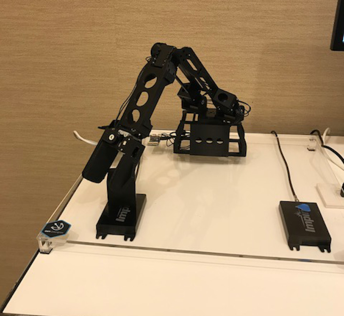 The image showcases a sophisticated black robotic arm positioned on a white surface, possibly within