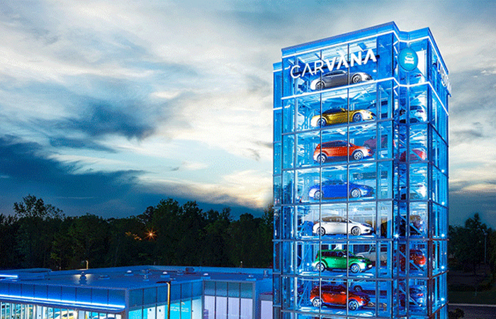 The image showcases the innovative Carvana car vending machine, a towering glass structure illuminated