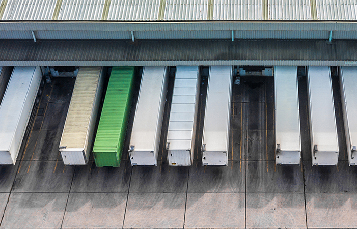 Aerial view of a neat line of white trucks docked at a warehouse with one green truck, illustrating Impinj's commitment to efficient logistics and user experience enhancement.