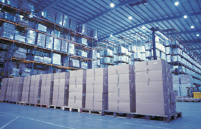 Inside a spacious and modern warehouse, stacks of neatly organized cardboard boxes are placed on