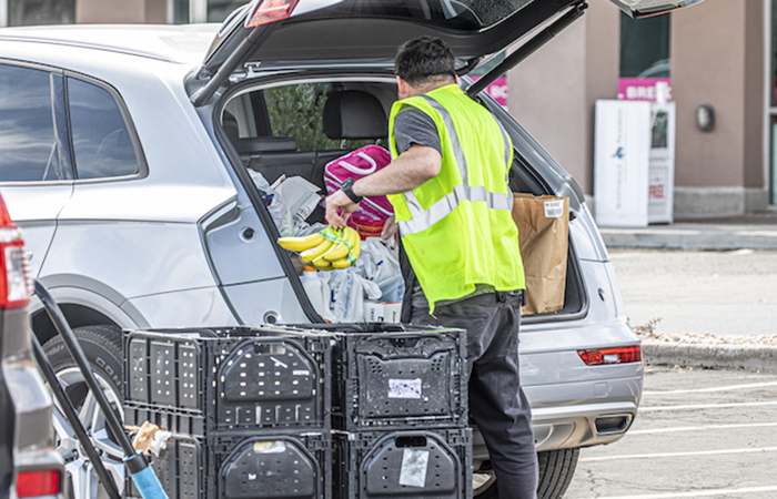 Curbside pickup service at a retail store with an employee loading groceries into a car trunk, illustrating Impinj's focus on improved user experience and convenience.