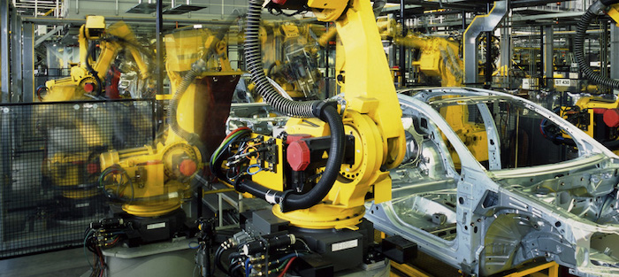 The image showcases a modern automotive assembly line where advanced yellow robotic arms are engaged in