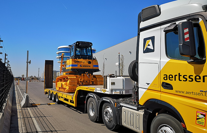Yellow Aertssen heavy haulage truck transporting an oversized construction excavator on an urban road, representing advanced logistics and website user personalization with Impinj technology.