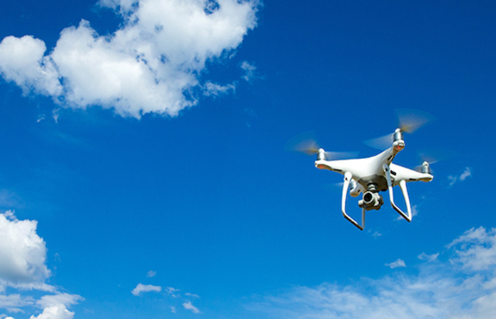 Quadcopter drone flying in a clear blue sky, symbolizing Impinj's innovative technology solutions.