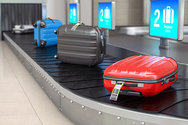 Colorful suitcases on an airport baggage claim conveyor belt with a focus on a red suitcase with a smart tracking tag.
