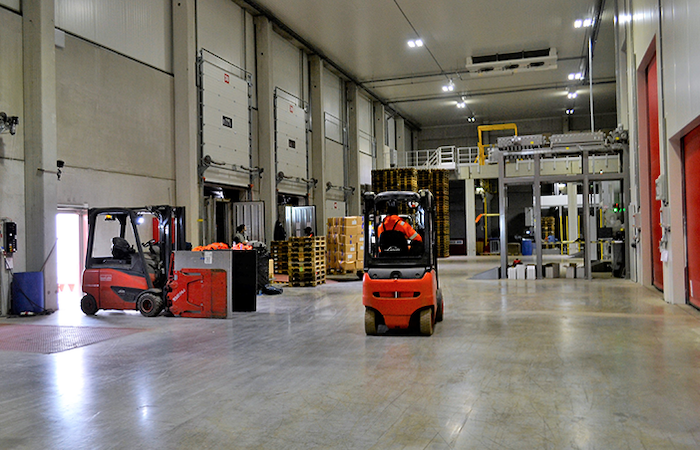 The image displays a bustling warehouse interior with two forklifts in operation,