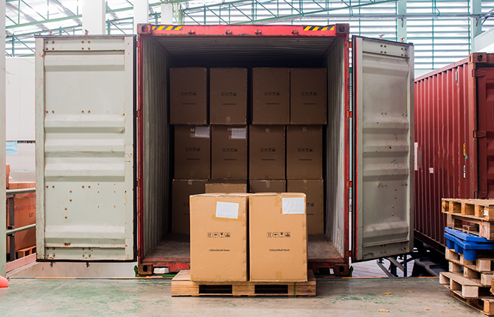 The image showcases a partially unloaded freight shipping container at a busy warehouse dock. The