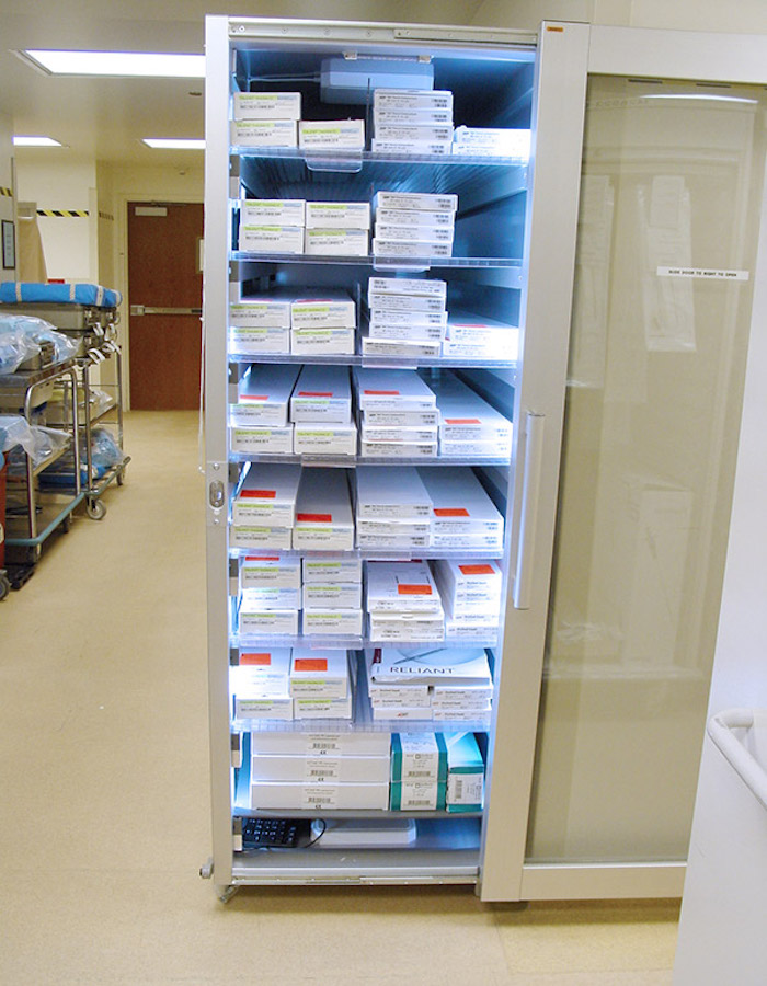 The image displays a well-organized medical supply cabinet, open and revealing numerous labeled