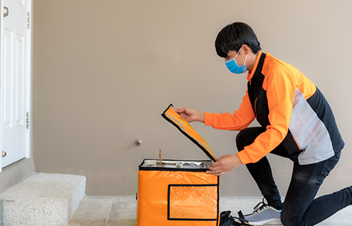 A technician in an orange and gray uniform is kneeling on a tiled floor next to