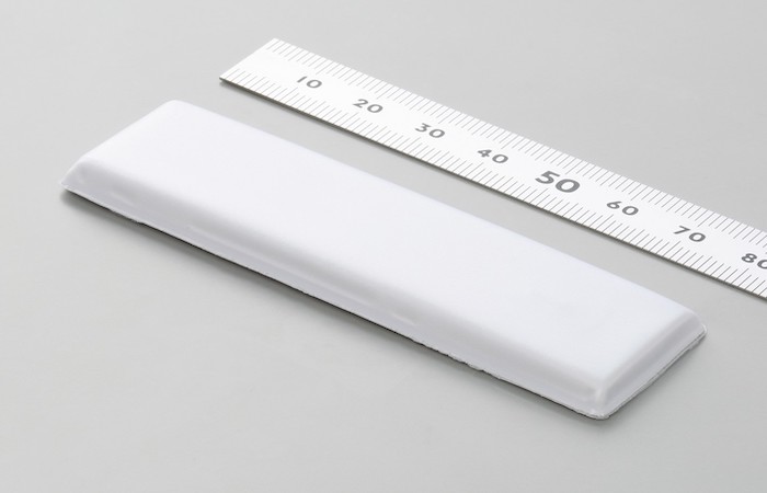 This image displays a pristine white Impinj RFID tag lying next to a stainless