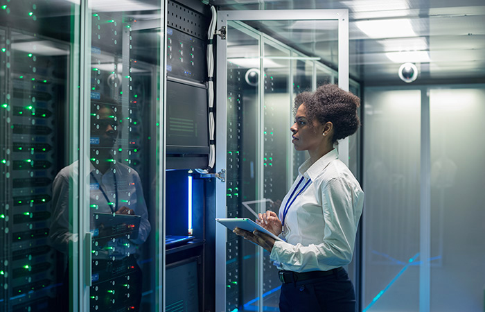 A professional in a white shirt and black pants is standing in a server room,