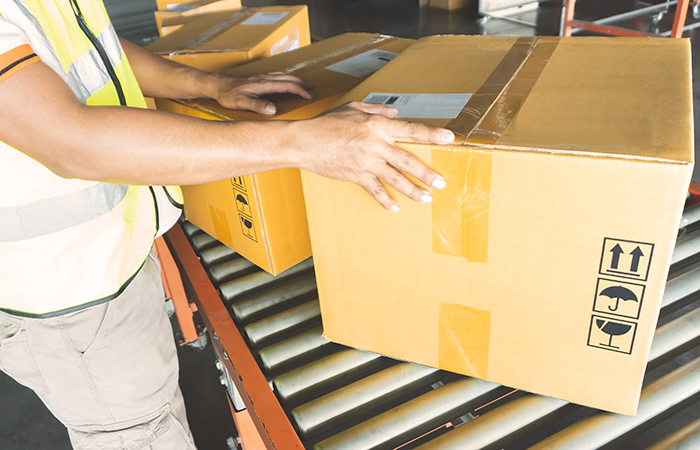 Warehouse employee managing a cardboard box on conveyor belt, demonstrating efficient package handling enabled by Impinj technology.