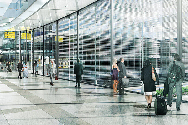 Passengers in a terminal standing in front of windows