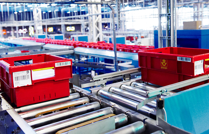 Red postal bins on a conveyor belt system in a modern distribution warehouse, showcasing efficient