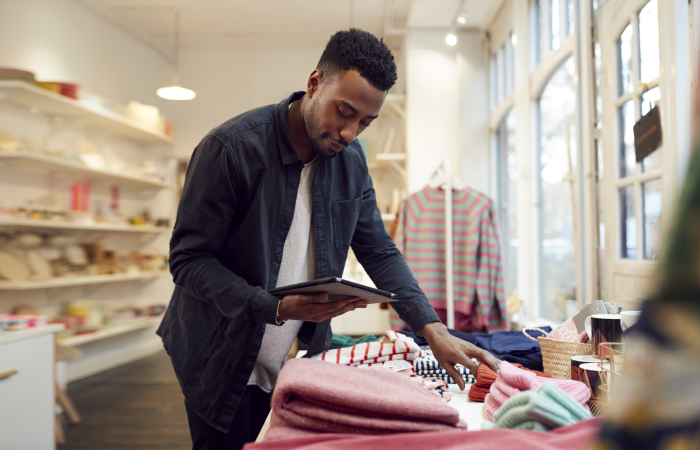 Retail worker using digital tablet for inventory management in a clothing store, embodying efficient operations consistent with Impinj's mission.