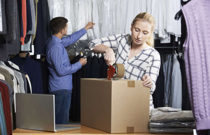 Employee packaging an order in a dry cleaning shop with a laptop and hanging garments