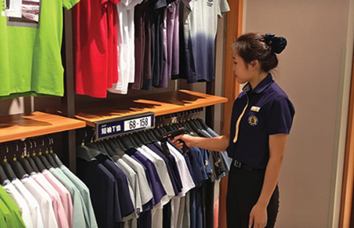 A retail employee in a uniform is using an Impinj RFID reader to scan
