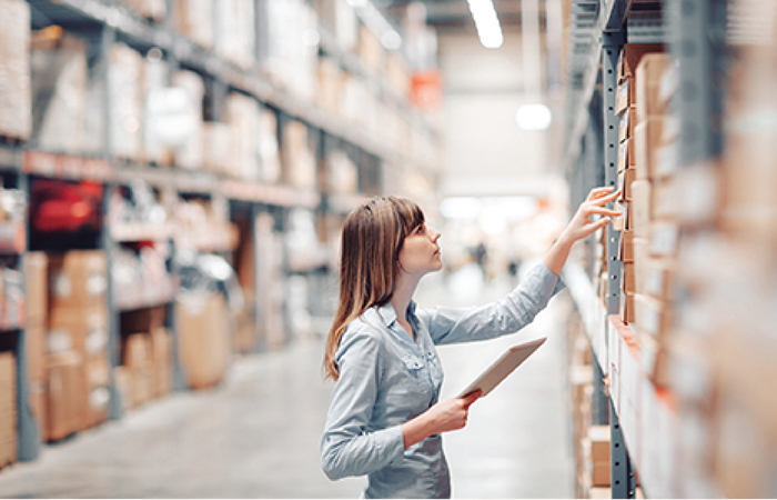 A warehouse employee in a gray shirt is checking inventory levels while holding a digital tablet