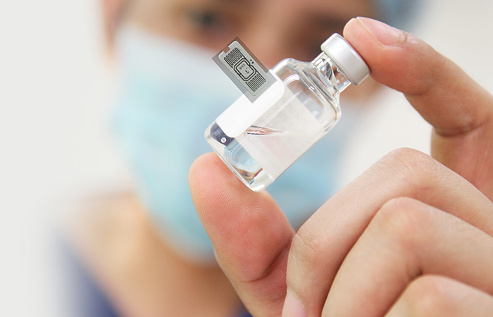 In the image, a healthcare professional wearing a surgical mask is holding a small glass