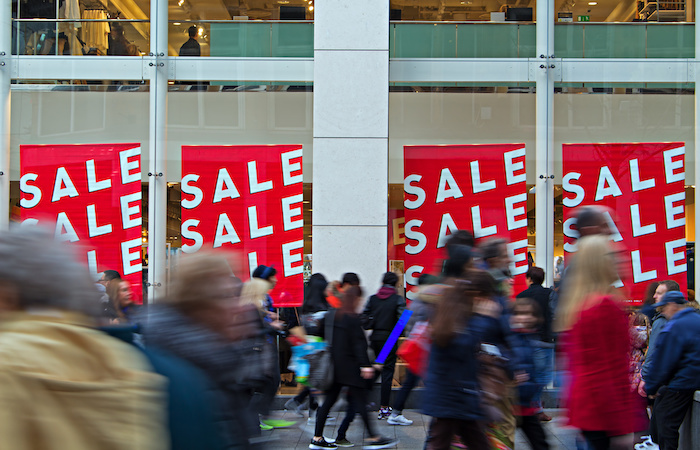 Shoppers rushing by a store with red 'SALE' banners during Black Friday, illustrating Impinj's commitment to enhancing user experiences