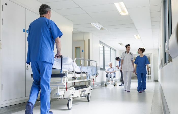 Healthcare professional in blue scrubs pushing an empty hospital bed in a corridor, reflecting Impinj's commitment to user experience and efficient healthcare service.