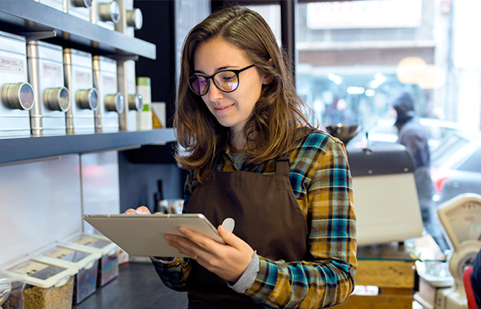 Retail worker in apron using digital tablet in an IoT-enabled store, aligning with Impinj's tech-forward approach