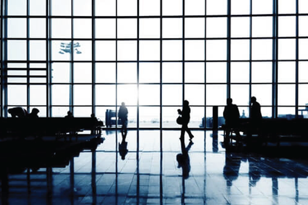 The image showcases a bustling airport terminal viewed through a large glass facade, casting sil