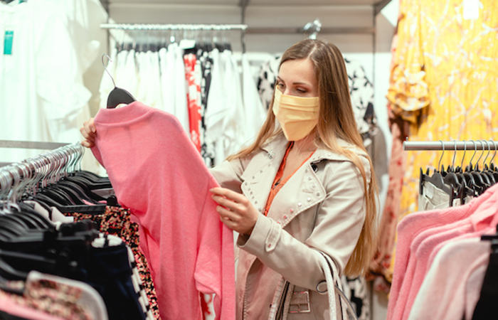 Customer shopping for clothes in a store, choosing a pink sweater, representing enhanced retail experience with Impinj technology