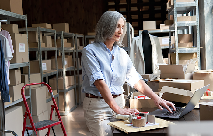 Warehouse employee organizing packages and using a laptop on a workstation, indicative of Impinj's inventory management solutions.