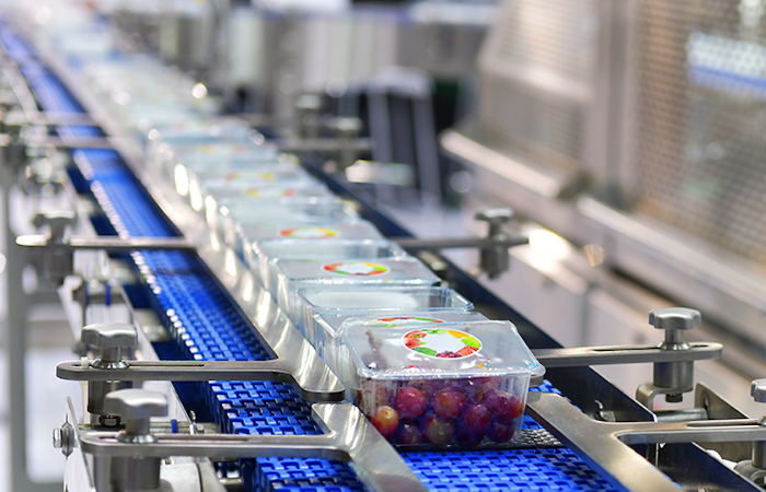 Transparent grape containers on a blue conveyor belt in a high-tech packaging facility, reflecting Impinj's efficient inventory management.