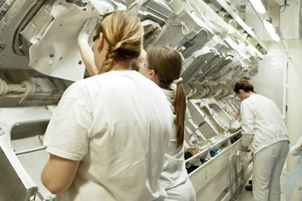 Three technicians in white lab coats are meticulously working on a large, complex piece of