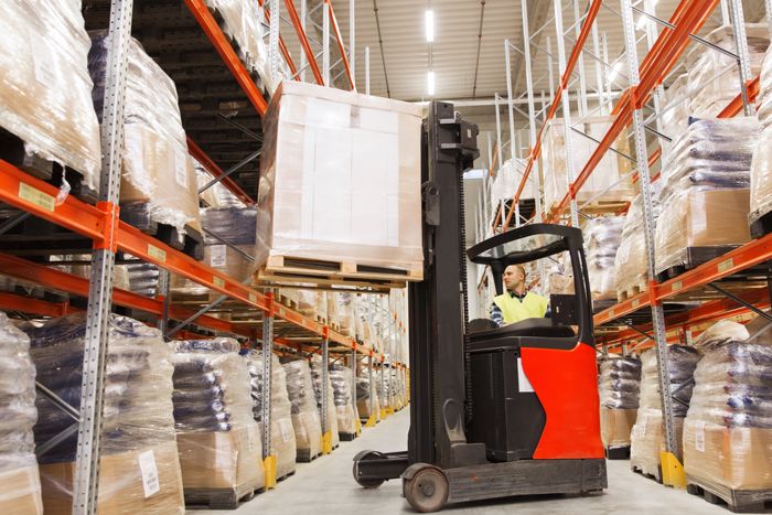 Warehouse operator driving forklift with pallet in an organized warehouse, illustrating Impinj's efficient inventory management solutions.