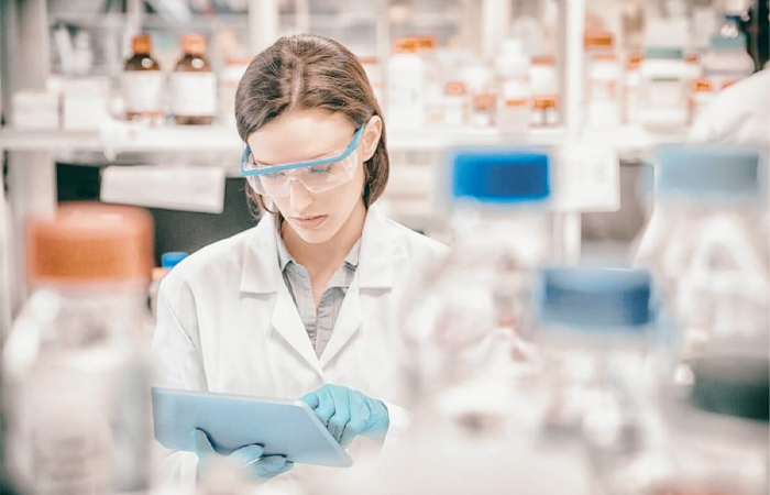 A professional researcher in a lab coat is meticulously reviewing data on a tablet within a