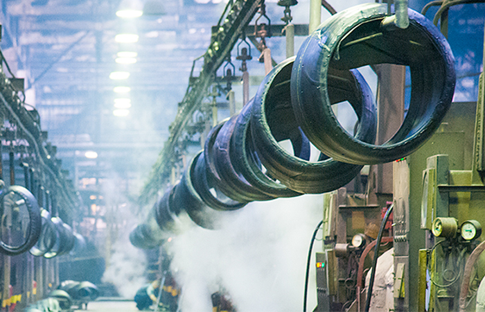 Inside a bustling industrial facility, large rubber tires are suspended from the ceiling amidst a