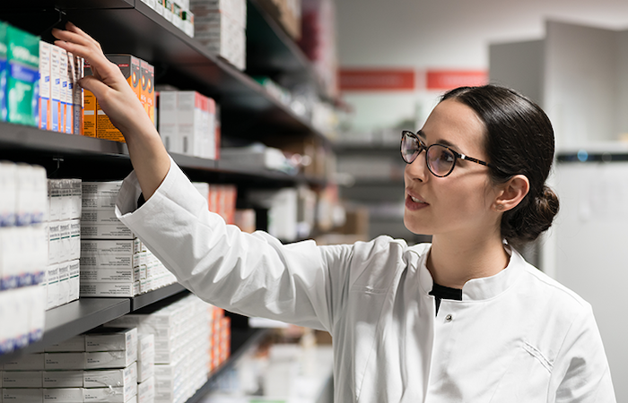 A pharmacist in a white coat is reaching for a medication box on a well-st