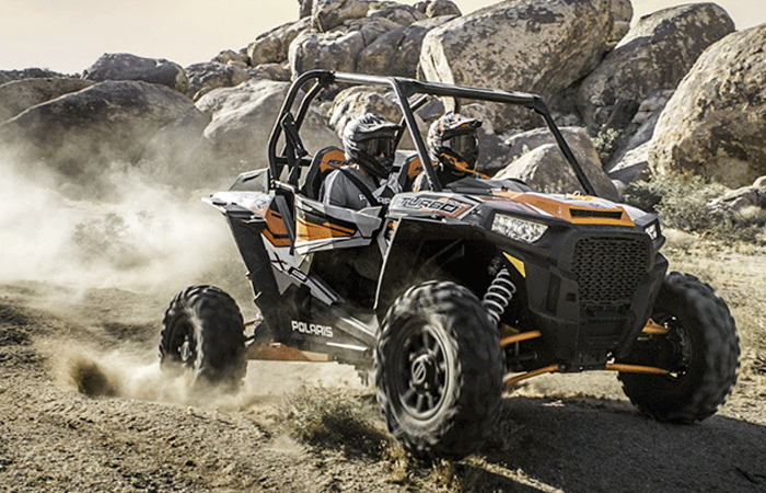 Two thrill-seekers are navigating a rugged desert terrain in a Polaris off