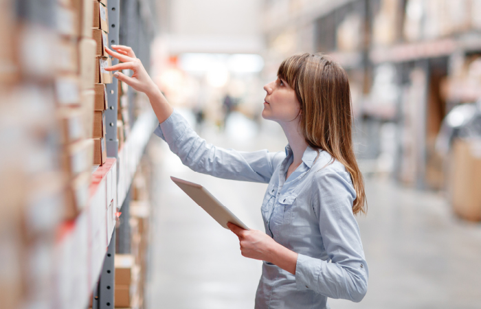 A professional woman in a warehouse setting is engaged in inventory management, holding a digital