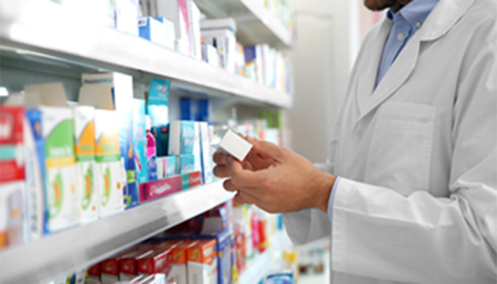 Pharmacist examining a medication box in a well-stocked pharmacy aisle, relevant to Impinj's user experience focus
