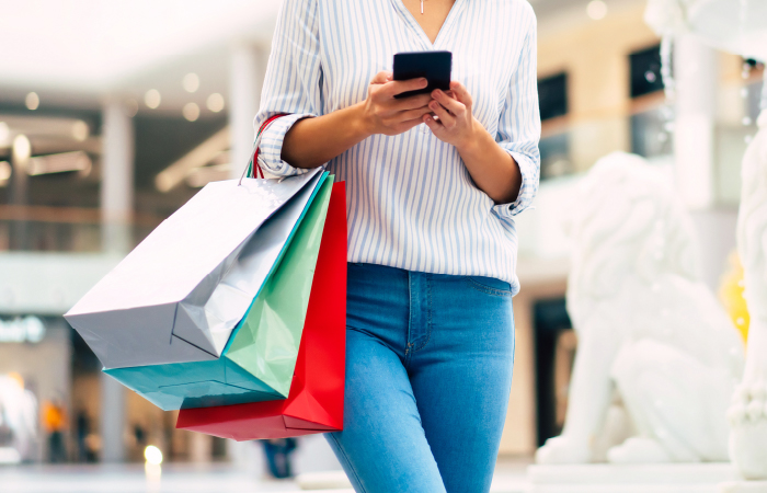 Woman with shopping bags using smartphone in mall, epitomizing Impinj's commitment to enhanced user experiences