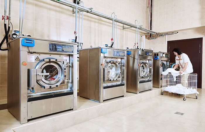 Worker loading laundry in industrial washing machines enhanced by Impinj technology