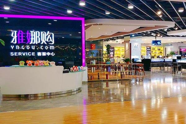 The image showcases a modern customer service desk with vibrant neon signage at a shopping center