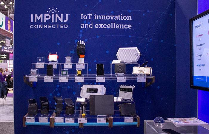 The image showcases a vibrant Impinj exhibition booth, highlighting their connected IoT (