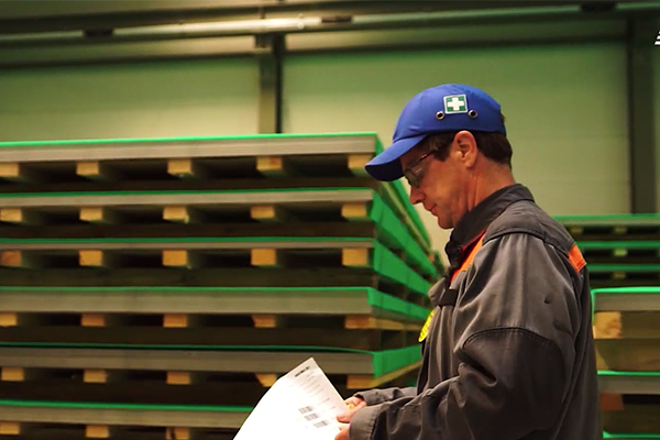 Empleado de almacén consultando lista en un entorno industrial, con estanterías de carga y palets verdes, representando la eficiencia operativa gracias a la tecnología de Impinj